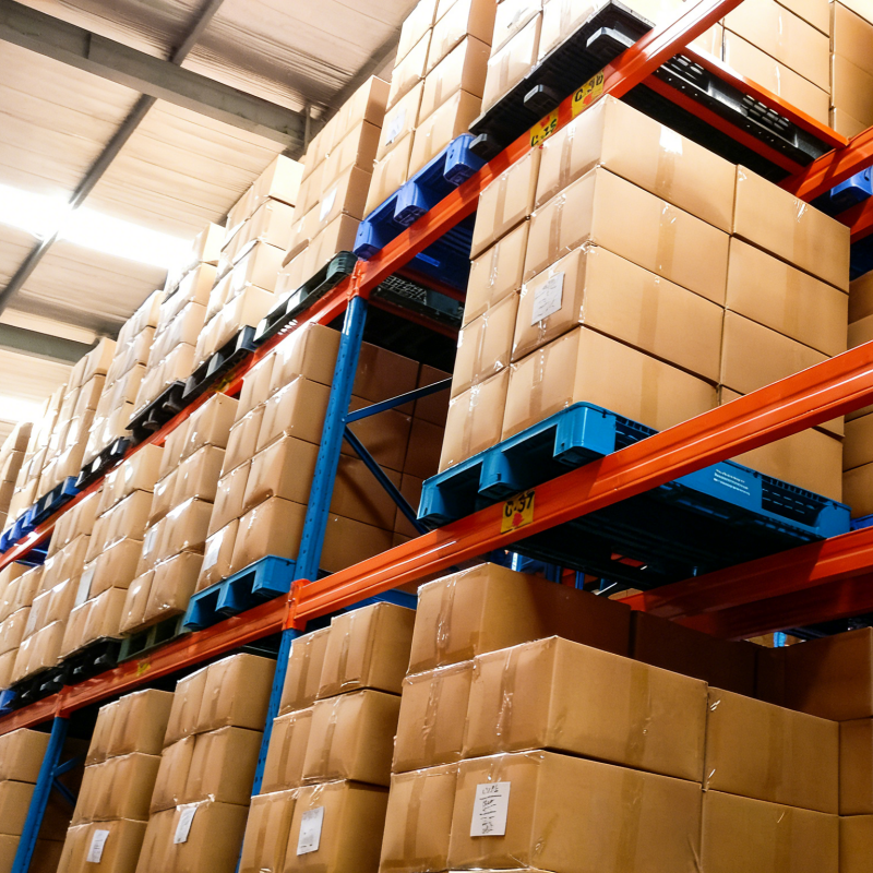 High-bay warehouse racking with blue pallets holding stacked cardboard boxes